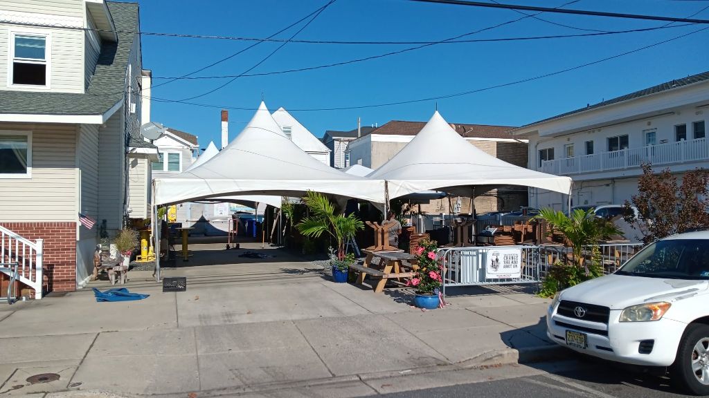 Cluster of connected white high-peak tents at a shore property with decorative plants