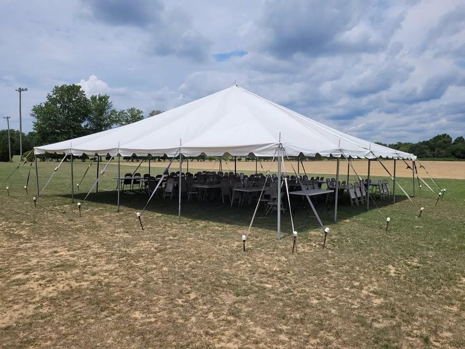 Large white pole tent set up on open field with round tables and folding chairs