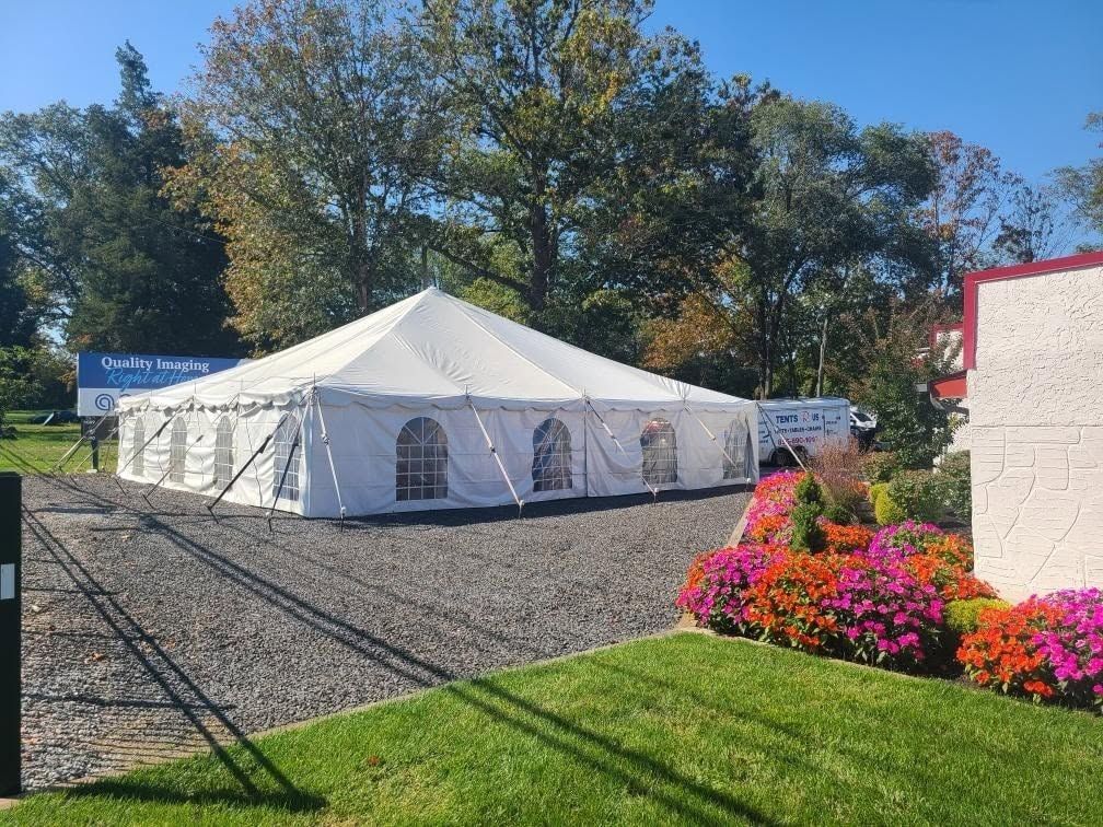 White pole tent with window sidewalls set up on gravel at a commercial property