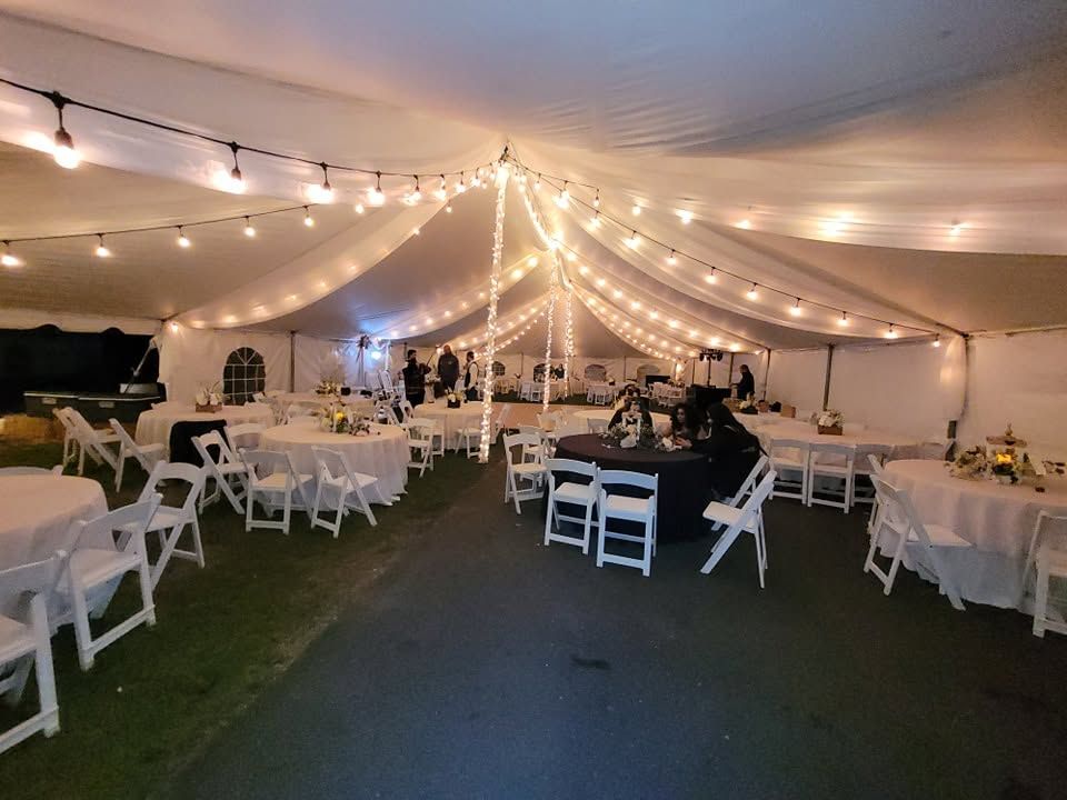 Inside a wedding tent at night with globe string lights, white chairs and round tables with floral centerpieces